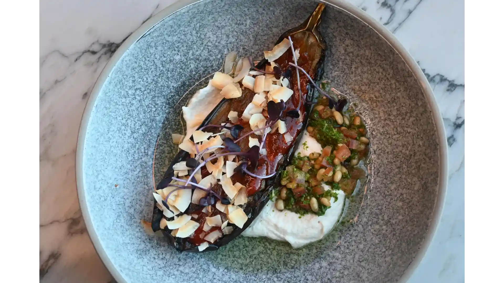 A beautifully crafted eggplant dish at Thirteen 50 Kitchen & Bar Auckland, glazed and topped with shaved coconut and microgreens, served alongside creamy purée and a vibrant herb dressing with pine nuts.
