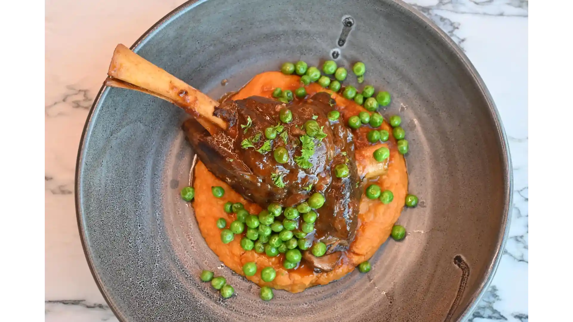 A hearty, slow-cooked lamb shank at Thirteen 50 Kitchen & Bar Auckland, glazed in rich gravy and served over creamy mash with a sprinkle of green peas for a comforting, flavour-packed dish.